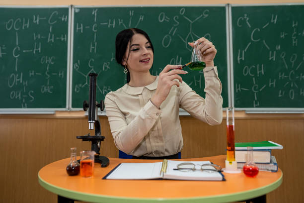 une étudiante pratique dans une classe de chimie avec des flacons sur un tableau avec des formules. - professor adult student chalk drawing formula photos et images de collection