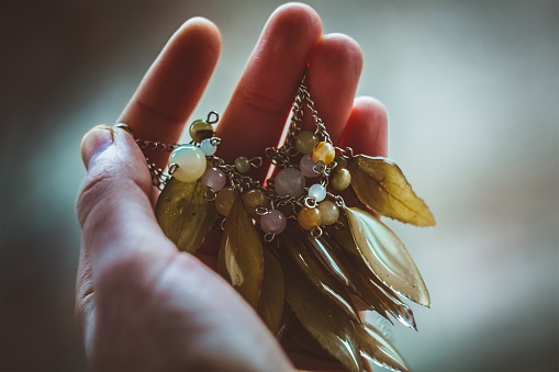 Close up woman holding bracelet with natural leaves concept photo. First view person photography with blurry background. High quality picture for wallpaper, travel blog, magazine, article