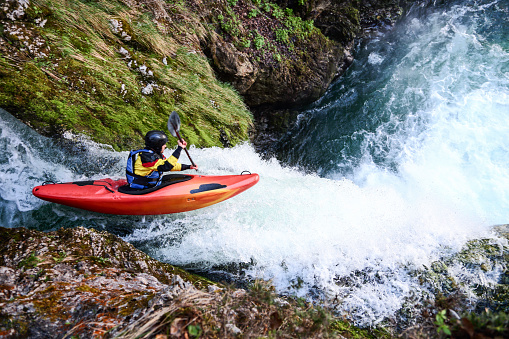 Man in red kayak going over a big waterfall. Extreme sports in nature. Danger on river.