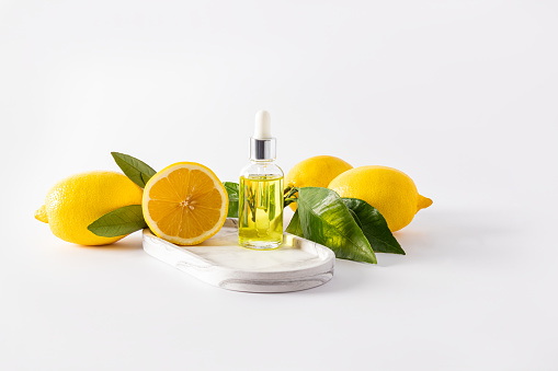 Cosmetic transparent bottle with a pipette with lemon serum for the face stands on a white tray with ripe fruits. natural cosmetics