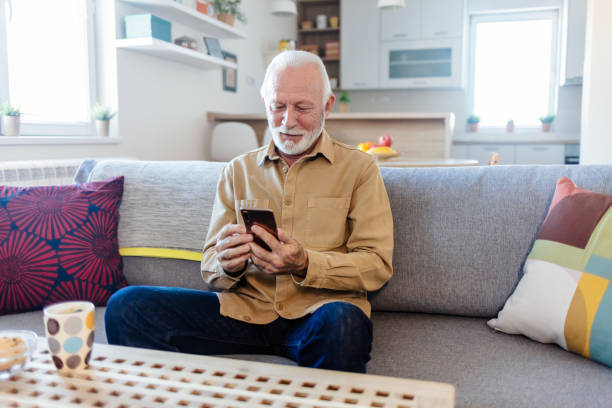 istock Shot of a senior man relaxing at home while using his smartphone. Senior man using a mobile phone in his living room. Internet and network concept. 1452484396