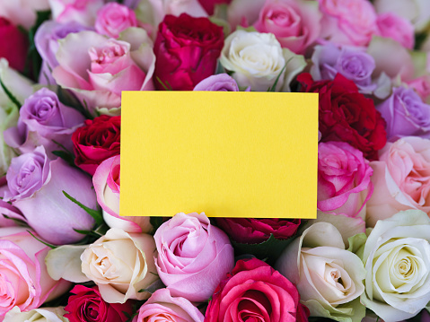 A yellow greeting card laying on a big bouquet of colorful roses