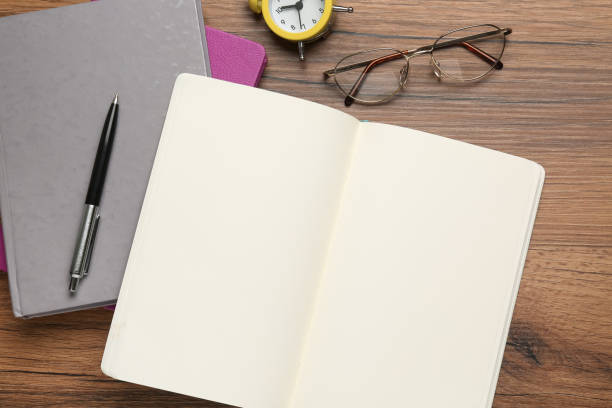 istock Notebooks, pen, glasses and alarm clock on wooden table, flat lay. Space for text 1452485573
