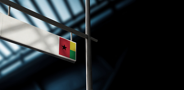 Flag of Guinea-Bissau on airport departure information board. Close-up. Roof construction in the background. Blue color. Horizontal orientation. Ne people. Copy space.