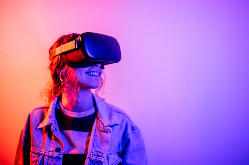 Young black woman playing game using VR glasses, enjoying 360 degree virtual reality headset for gaming, isolated on background with neon lights