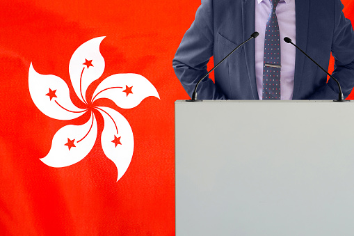 Tribune with microphone and man in suit on Hong Kong flag background. Businessman and tribune on Hong Kong flag background. Politician at the podium with microphones background Hong Kong flag