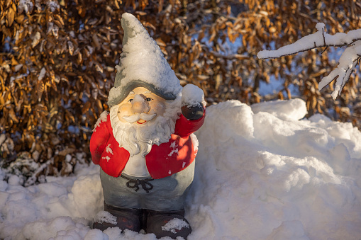 Beautiful view of figure of gnome standing in snow covered garden on sunny frosty winter day. Sweden