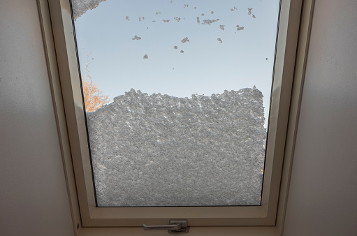 Close up view of interior of snow-covered dormer window on roof of house from room covered with snow on frosty winter day. Sweden.