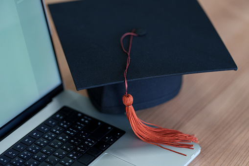 Graduation cap with laptop pace on wood table background.