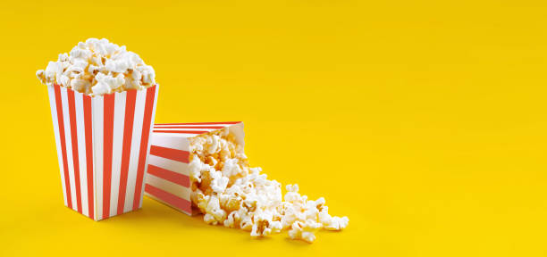 Cтоковое фото Два красно-белых полосатых картонных ведра с вкусным сырным попкорном, изолированные на желтом фоне
