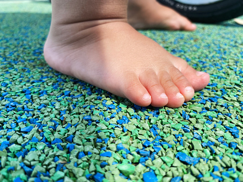 Baby feet on playground. Child barefoot on perforated playground. Padded floor covering with rubber granules.