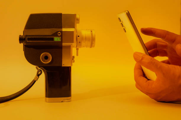 コンテンツクリエーターは、オレンジ色の照明でスマートフォンで古い8mmフィルムカメラを撮影しています。消費者の便宜を図った撮影。 - director film industry camera old fashioned ストックフォトと画像