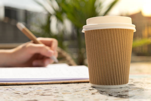 istock Unrecognizable Young woman study in beach resort. Drinking coffee from paper cup. Student making homework Female hands writing on notebook gratitude journal self reflection self discovery in Co-Working Space. Goals, to-do list Remote 1452497719