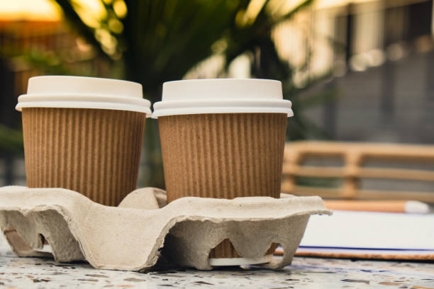 istock Two paper cups with lid for tea to go. Coffee take away on the table. Take-out coffees with brown paper cup holder. Brown safety cardboard collars. Cardboard tray 1452497760