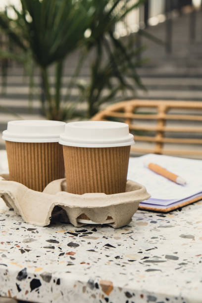 istock Two paper cups with lid for tea to go. Coffee take away on the table. Take-out coffees with brown paper cup holder. Brown safety cardboard collars. Cardboard tray 1452497835