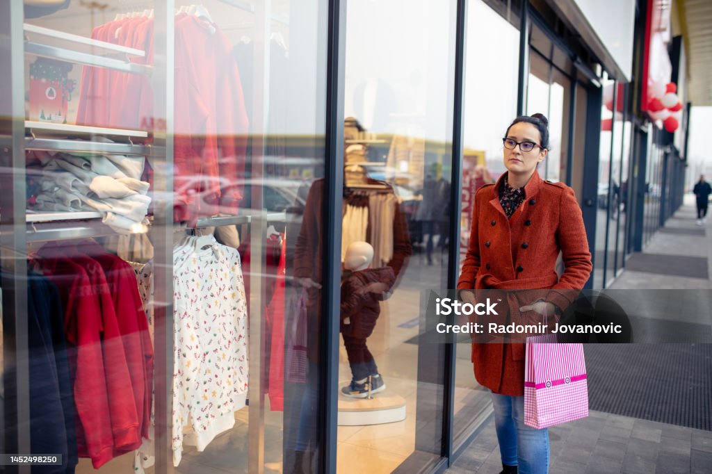 Woman Window Shopping Woman walking outdoors in a city. She is window shopping and looking at a store sale advertising or marketing apparel and clothing on a display glass. Adult Stock Photo