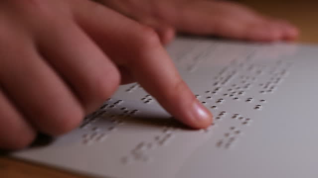 Close up on braille text, fingers of a young girl reading.