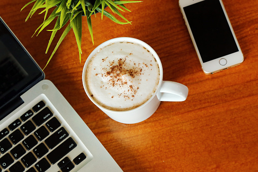 Hot Latte on wooden table in cafe with laptop and smartphone. Hot Chocolate on desk have computer notebook and mobile phone background.