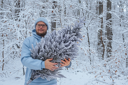 cheerful man holds snowy Christmas tree in hands
