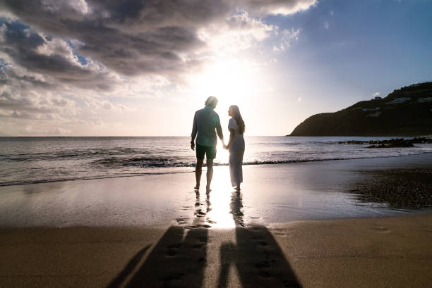 sylwetka młodej pary zaręczonej trzymającej się za ręce podczas zachodu słońca na piaszczystej plaży na wyspie - men footprint beach sunset zdjęcia i obrazy z banku zdjęć