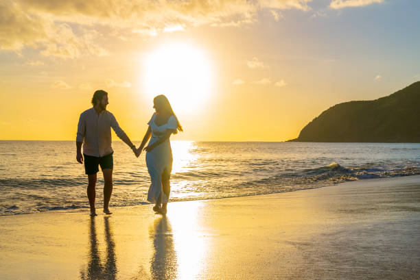istock Young couple walking along sandy beach away from the sunset 1452510716