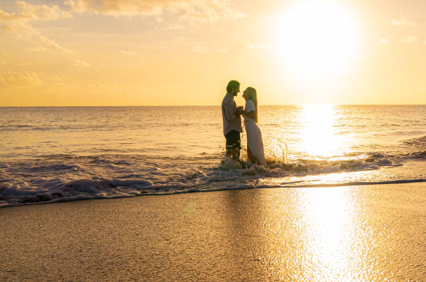 istock Young well-dressed couple holding hands as ocean waves crash into them on a sandy beach during the sunset 1452510717
