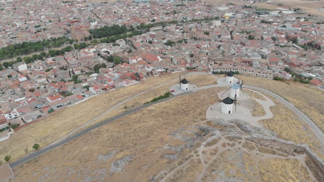 Aerial drone panning left wide shot over white windmills with city laying behind (Consuegra, Toledo)