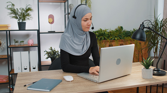 Businesswoman working on laptop computer wearing headset, freelance worker call center, support service operator helpline, having pleasant talk with client or colleague communication support at office
