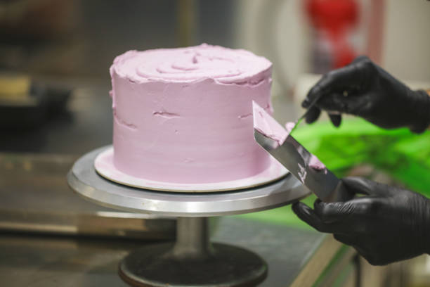 istock Decorator using spatula and scraper smoothing lilac buttercream birthday frosted cake 1452514010