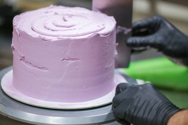 istock Decorator using spatula and scraper smoothing lilac buttercream birthday frosted cake 1452514012