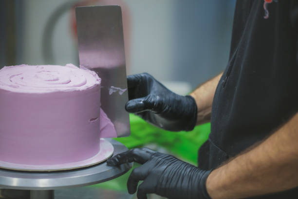 istock Decorator using spatula and scraper smoothing lilac buttercream birthday frosted cake 1452514016