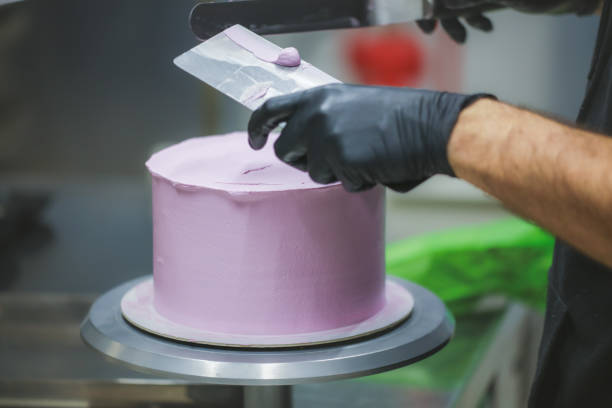istock Decorator using spatula and scraper smoothing lilac buttercream birthday frosted cake 1452514054