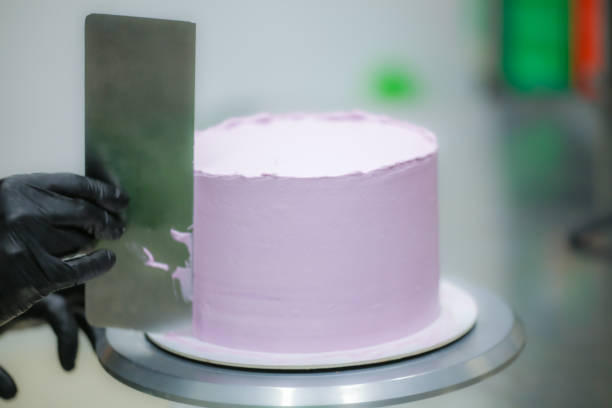 istock Decorator using spatula and scraper smoothing lilac buttercream birthday frosted cake 1452514067
