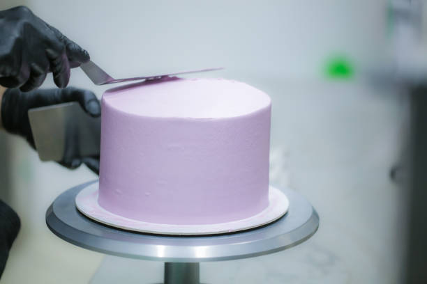 istock Decorator using spatula and scraper smoothing lilac buttercream birthday frosted cake 1452514084