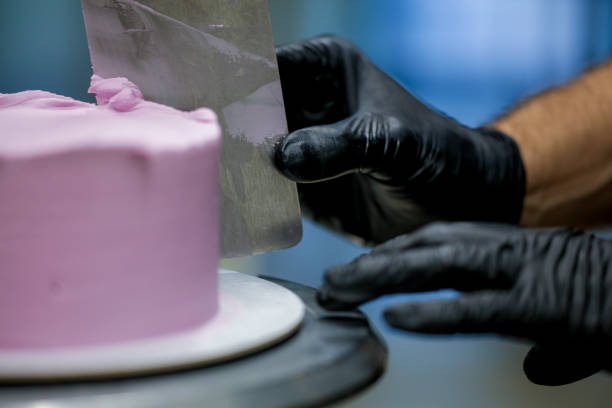 Decorator using spatula and scraper smoothing lilac buttercream birthday frosted cake