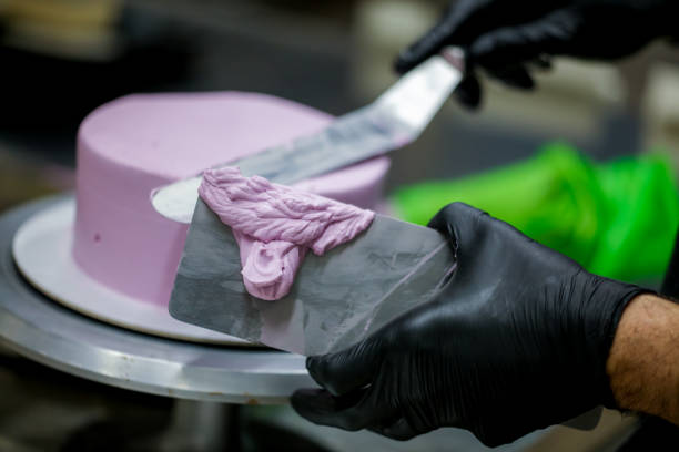 istock Decorator using spatula and scraper smoothing lilac buttercream birthday frosted cake 1452514131