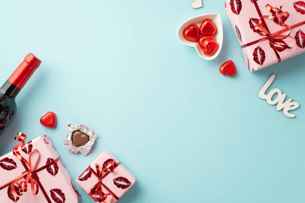 valentine's day concept. top view photo of gift boxes in wrapping paper with kiss lips pattern wine bottle and heart shaped dish with chocolate candies on isolated light blue background with copyspace - valentines day candy chocolate candy heart shape imagens e fotografias de stock