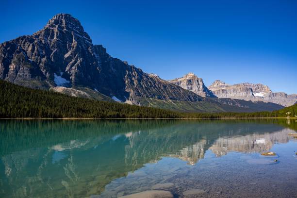 istock A transparent mountain lake's surface, with a forest and snowy mountain slopes in the background 1452516992