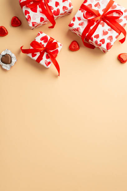 saint valentine's day concept. top view vertical photo of gift boxes in wrapping paper with heart pattern and chocolate candies on isolated pastel beige background with copyspace - valentines day candy chocolate candy heart shape imagens e fotografias de stock