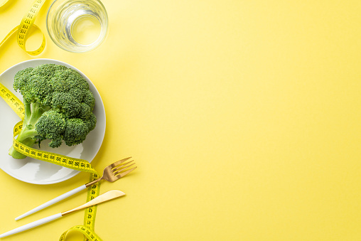 Slimming concept. Top view photo of plate with cauliflower glass of water measuring tape knife and fork on isolated pastel yellow background with copyspace