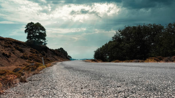 vista del cielo, los árboles, los maquis y las nubes a lo largo de una carretera asfaltada desgastada en una ciudad del egeo - country road lane road dirt road fotografías e imágenes de stock