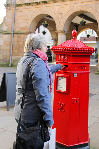 Woman posting letter into mail box in Shrewsbury Shropshire, hoping that the Royal mail strikes will not prevent it reaching its destination.