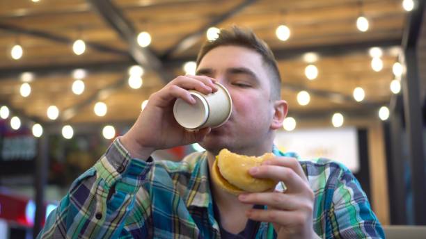 istock Hungry man is actively eating a burger. A young man in a cafe eats a burger and drinks coffee. Close-up of a man's face. 1452526541