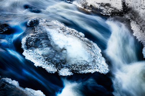 Stone in a river with an ice cap, flowing water under photographed with long exposure to make water hazy and dreamy