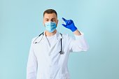 young doctor in medical mask and white coat with stethoscope holding syringe isolated on blue