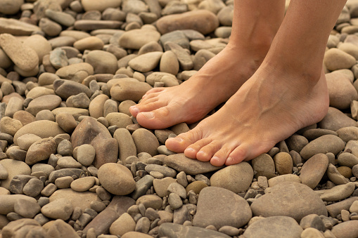 Woman feet walking on sea pebbles. Natural foot massage. Beauty and body care. Healthy lifestyle. Vacation and rest