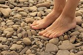 Woman feet barefoot stand on a sea pebble
