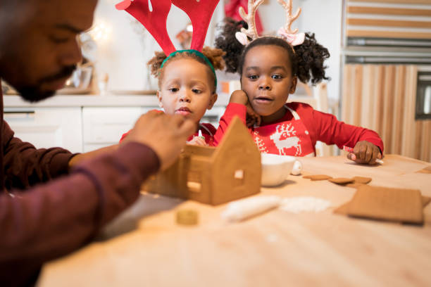 African American family decorating a gingerbread house together on Christmas day. Christmas moments with kids at home concept. Selective focus