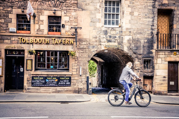 Edinburgh, Scotland - July 14, 2022: Senior bicyclist passing by the old tavern on Royal Mile in Edinburgh.