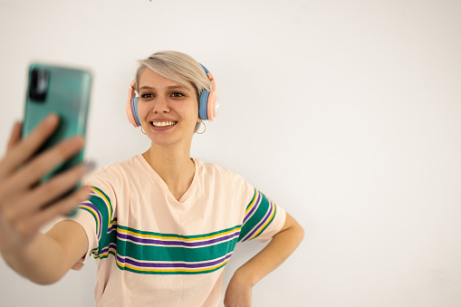 Studio portrait of a happy young woman listening to music and taking a selfie